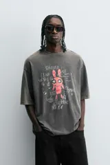 Camiseta gris con efecto lavado, cuello redondo y manga corta. Estampado frontal con conejo, texto y efecto de pintura.