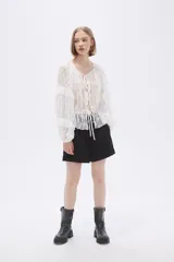 Blusa blanca traslúcida de encaje con mangas largas abullonadas y volados.
