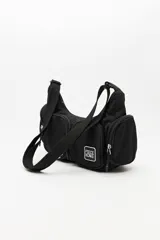 Cartera tipo shoulder color beige, de diseño utilitario y formato curvo. Confeccionada en material liviano y resistente, cuenta con correa regulable para llevar al hombro o cruzada. Presenta múltiples bolsillos con cierre en el frente y laterales, y un parche con el logo "Piece & Cake" en el frente.