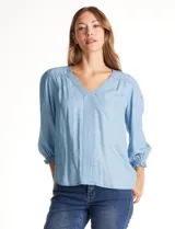 Blusa de lyocell color azul claro, con escote en V, detalles de costuras verticales en el frente y mangas tres cuartos con puños elastizados.