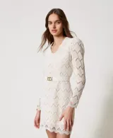 Vestido corto color blanco de encaje macramé con diseño geométrico, escote de pico, mangas largas abullonadas tipo guante con cremallera invisible en el bajo, cierre de cremallera en el lateral, bajo festoneado, forro de muselina de algodón y cinturón extraíble a juego con elástico y hebilla con el logotipo Oval T dorado, de corte recto.