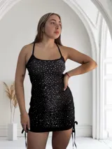 Minivestido negro ajustado al cuerpo, con escote recto y breteles finos. Decorado con strass plateados.