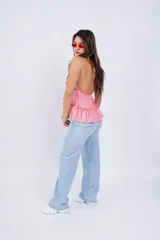 Top rosa con escote halter, volados en el cuello y en el ruedo, y lazo ajustable en el frente.