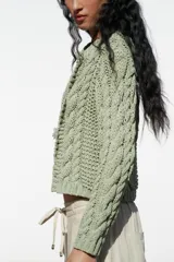Chaqueta de punto color verde claro, con cuello redondo y manga larga. Cierre frontal con botones a presión en forma de flor.