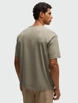 Camiseta negra de corte relajado con cuello redondo y manga corta. Presenta un diseño tridimensional en el pecho que simula un pliegue o estructura geométrica en tono negro brillante o texturizado.