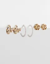 Set de tres pares de aros dorados: argollas con moño, argollas con perlas y aros pasantes con forma de flor.