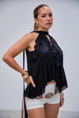 Blusa negra con cuello halter y escote en V, adornada con volados en el frente y en el bajo. Diseño asimétrico y tiras largas que caen por la espalda.