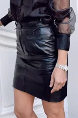 Minifalda negra de cuero con corte recto, pretina ancha con trabillas y bolsillo trasero de parche.