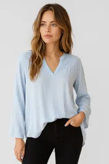 Blusa celeste de viscosa con cuello en V y mangas largas. Presenta detalles de broderie en los hombros y corte holgado.