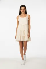 Vestido corto color crema, de breteles finos con borlas, corte holgado y falda escalonada.