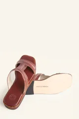 Sandalias bajas de cuero color marrón con costuras blancas a la vista.