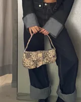 Cartera tipo baguette con estampado animal print en tonos marrones y verdes, con asa corta y cierre con hebilla metálica.