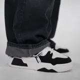 Zapatillas urbanas de plataforma, color blanco y negro, con diseño robusto y detalles de salpicaduras de pintura negra en el lateral.