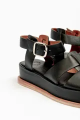 Sandalias negras de cuero con plataforma y tiras cruzadas en el empeine y tira con hebilla alrededor del tobillo.