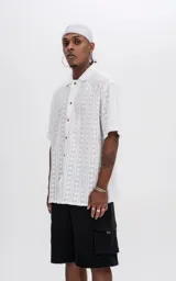 Camisa blanca con textura y botones marrones, de corte holgado y mangas cortas.