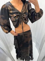 Top corto negro con estampado abstracto en tonos dorados, escote en V con frunce regulable y mangas largas abullonadas con puños elásticos.