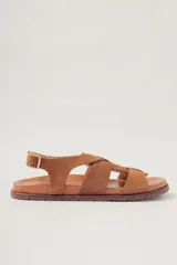 Sandalia plana de gamuza color camel, con tiras cruzadas en la parte delantera y tira ajustable con hebilla en el tobillo. Posee plantilla de cuero y suela de goma.