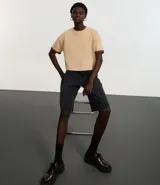 Blusa color beige, cropped y de corte amplio, confeccionada en tejido de media malla, con cuello redondo y mangas cortas.