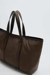 Bolso tipo shopper color marrón, fabricado en tejido de algodón con detalles en piel. Asas fabricadas en piel y algodón. Compartimento principal con cierre mediante imán. El interior cuenta con un bolsillo con cierre mediante cremallera y un bolsillo plano.