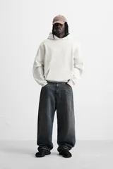 Sudadera con capucha gris confeccionada en tejido de algodón con interior rizo. Tiene manga larga, bolsillo frontal tipo canguro y acabados en rib.