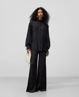 Camisa blanca de manga larga, con cuello chimenea alto y botonadura frontal oculta. El tejido es semitransparente y presenta una textura ligera.