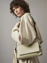 Cartera de hombro color crema, marca Calvin Klein, modelo CK Must. Tiene correa de hombro ajustable con el logo de la marca y otra correa más fina.