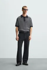 Polo de hombre de corte relajado, tejido de punto de algodón a rayas verticales en tonos gris y negro. Tiene cuello solapa, cierre frontal con botones y mangas cortas.