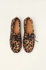 Mocasín tipo boat shoe con estampado de vaca en tonos marrón y blanco, confeccionado en cuero. Cuenta con cordones de cuero marrón oscuro y suela de goma.