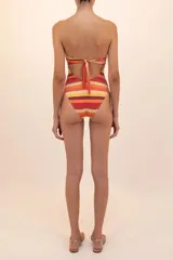 Traje de baño entero bandeau a rayas horizontales en tonos naranja, amarillo y borgoña, con aro dorado metálico y cut out en el centro del busto.