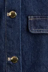 Campera de denim azul con cuello redondo, cierre frontal con botones dorados y cuatro bolsillos de parche con solapa y botón.