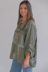 Blusa verde militar con estampado abstracto en tonos grises y marrones, de corte holgado y mangas 3/4 con botón para sujetar.