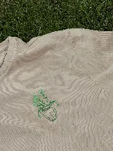 Remera color beige con cuello redondo y estampado de un jarrón con flores en color verde.