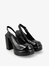 Zapato de tacón negro de charol, con punta redonda, plataforma delantera y correa con hebilla en el tobillo.