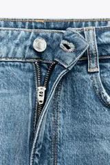 Pantalón de jean gris oscuro, de corte mom fit, tiro alto y largo tobillero. Cuenta con cinco bolsillos, cierre frontal con cremallera y botón.