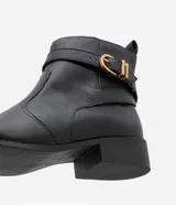 Bota de cuero negro con puntera redonda, caña corta con tirador, cierre lateral con cremallera y detalle de hebilla dorada con doble trabilla.