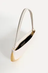 Bolso de hombro alargado color crema, con asa corta y detalle metálico dorado en un lateral. Tiene un bolsillo interior con cremallera y cierre principal con cremallera.