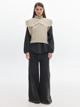 Chaleco de punto color beige con cuello alto y pechera desmontable con flecos.