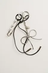 Llavero con aro metálico plateado, moño metálico plateado, cadena metálica plateada con dije de perla, alfiler de gancho plateado con perlas, cordón de cuero negro y aros de plástico blanco y negro.