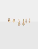 Set de tres pares de aros dorados: un par de aros tipo botón con forma de corazón, un par de aros tipo argolla con dije de corazón con strass y un par de aros tipo argolla con strass.