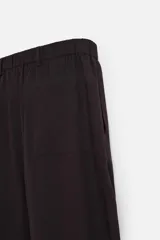 Pantalón relaxed fit color marrón oscuro confeccionado en tejido con mezcla de algodón y lino. Cintura elástica, bolsillos laterales y bolsillo trasero de plastrón. Perneras con pliegues frontales. Cierre en delantero con cremallera y botón.