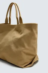 Bolso tipo shopper color beige confeccionado en piel con acabado serraje. Cuenta con doble asa de mano y compartimento principal con cierre magnético. El interior tiene un bolsillo con cierre de cremallera.