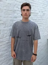 Remera gris oscuro con efecto acid wash, corte oversize y manga corta. Presenta un estampado minimalista en negro con texto que incluye "TRUTH IS A STATE OF MIND" y un logo gráfico.