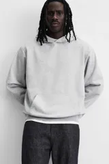 Sudadera con capucha gris confeccionada en tejido de algodón con interior rizo. Tiene manga larga, bolsillo frontal tipo canguro y acabados en rib.