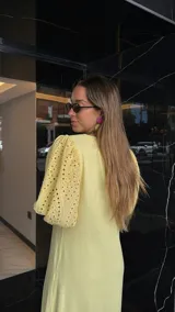 Vestido largo color amarillo pálido, con escote en V, mangas cortas abullonadas con detalle de calado y ruedo con volantes y calado.