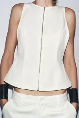 Top de denim color blanco, de cuello redondo y sin mangas. Cierre frontal con cremallera metálica.