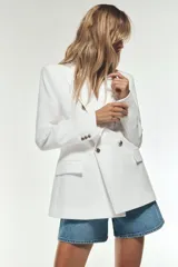 Blazer color blanco hueso, de corte entallado y doble botonadura dorada. Tiene cuello con solapa, mangas largas con hombreras y bolsillos delanteros con solapa.