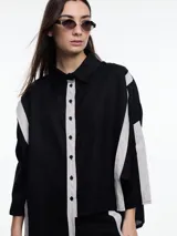 Camisa de lino color negro con silueta amplia y mangas 3/4. Diseño con tiras de color blanco en contraste en la cartera, mangas y cuerpo. Tiene tajos laterales y ruedo irregular en el frente.