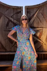 Vestido largo de poliéster con estampado floral en tonos celeste, amarillo y rosa. Diseño cruzado con escote en V y mangas cortas con volados.