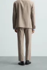 Pantalón de vestir para hombre, color beige claro con textura de tejido de lana. Presenta un corte regular fit, con pliegues marcados en el frente, bolsillos laterales y bolsillos traseros de doble vivo con botón.