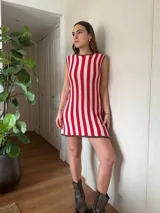 Vestido corto de algodón tejido en punto jersey con diseño de rayas verticales rojas y blancas. Terminaciones en crochet hechas a mano con detalle de lurex. Cuello redondo, sin mangas y silueta trapecio.